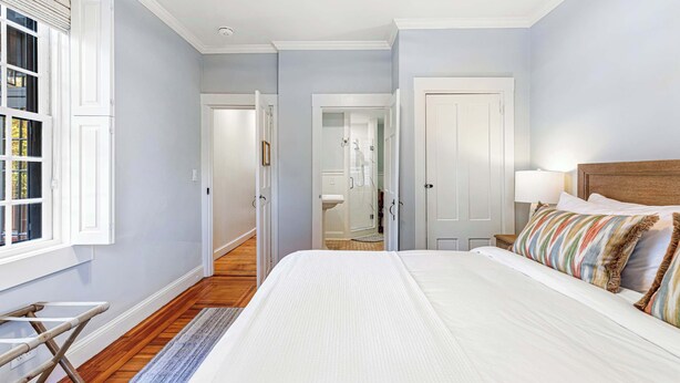 A bedroom with a large bed, a wooden floor, a window with blinds, and a door leading to a bathroom. - The Royce on Spring - High-end Family Getaway in Newport (Newport)