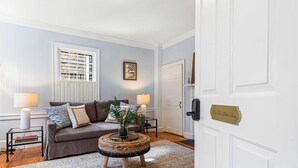A living room with a brown sofa, two side tables with lamps, a woven coffee table, and a patterned rug. - The Royce on Spring - High-end Family Getaway in Newport (Newport)