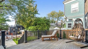 A wooden deck with a lounge chair and a wicker chair, surrounded by a black railing. - Sea Glass Suite - Luxury in Newport (Newport)