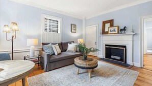 A living room with a grey sofa, a round coffee table with a plant, a fireplace, and a white door. - Sea Glass Suite - Luxury in Newport (Newport)