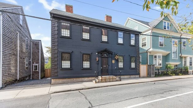 A two-story building with a dark blue exterior, a front entrance with a small porch, and a visible street view. - Sea Glass Suite - Luxury in Newport (Newport)