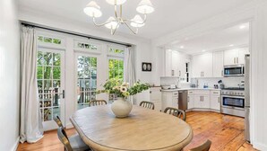 A modern kitchen with white cabinetry, a central island, and a dining area with a wooden table and chairs. - Sea Glass Suite - Luxury in Newport (Newport)