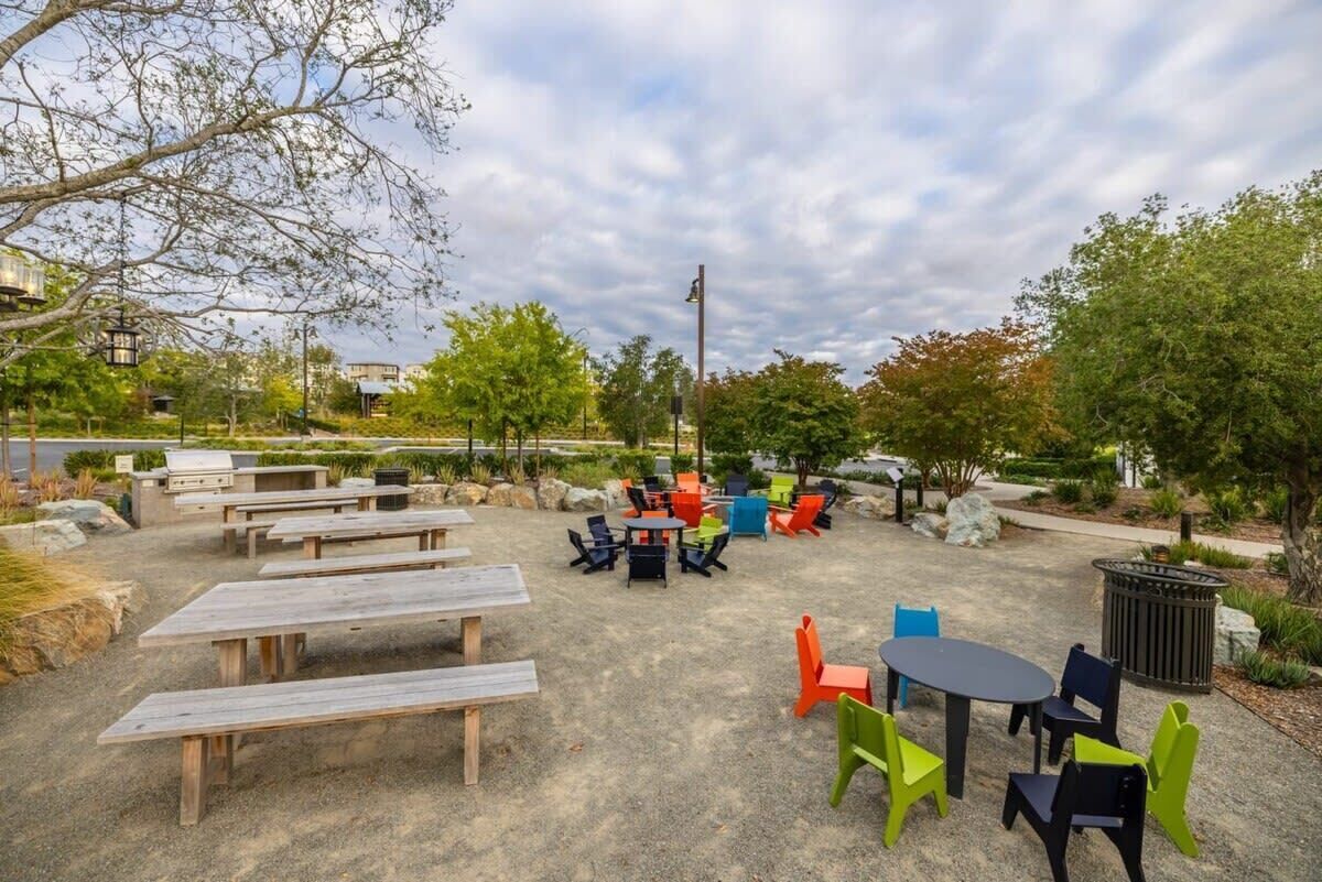 An outdoor seating area with picnic tables and chairs, surrounded by greenery and trees.
