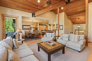 A spacious living area with a high ceiling, wooden beams, a dining area, and a kitchen. - Wallowa 22 (Bend)