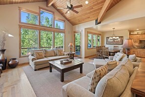 A spacious living room with a high ceiling, large windows, a fireplace, and a dining area. - Wallowa 22 (Bend)