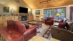 A cozy living room with a fireplace, leather sofas, a flat-screen TV, and a large window with a view of trees. - Tamarack 8 (Bend)