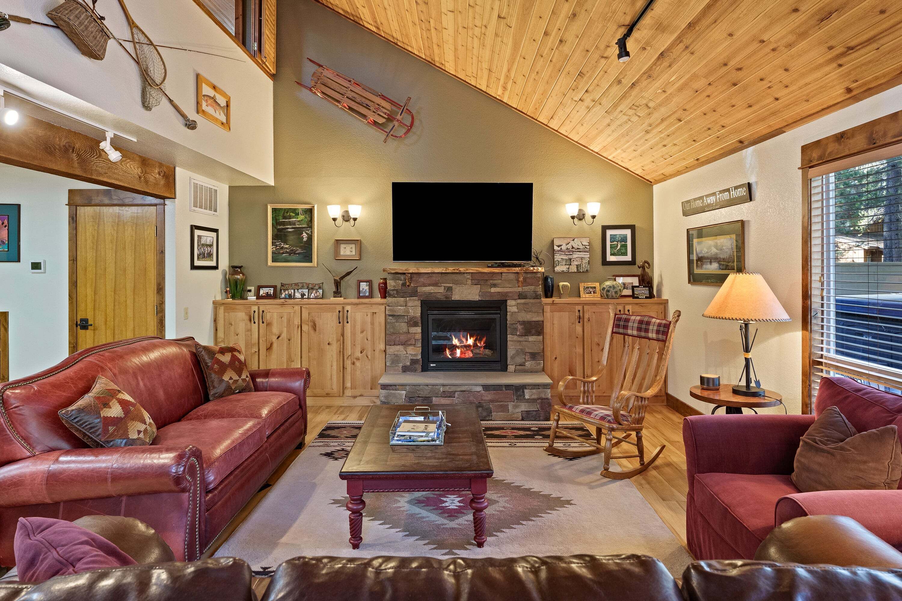 Un salón acogedor con chimenea, sofás de cuero, un televisor de pantalla plana y techos de madera.
