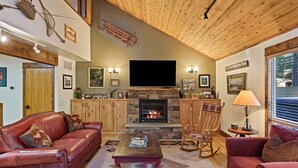 A cozy living room with a fireplace, leather sofas, a flat-screen TV, and wooden ceilings. - Tamarack 8 (Bend)
