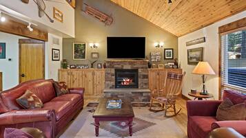 Un salón acogedor con chimenea, sofás de cuero, un televisor de pantalla plana y techos de madera.