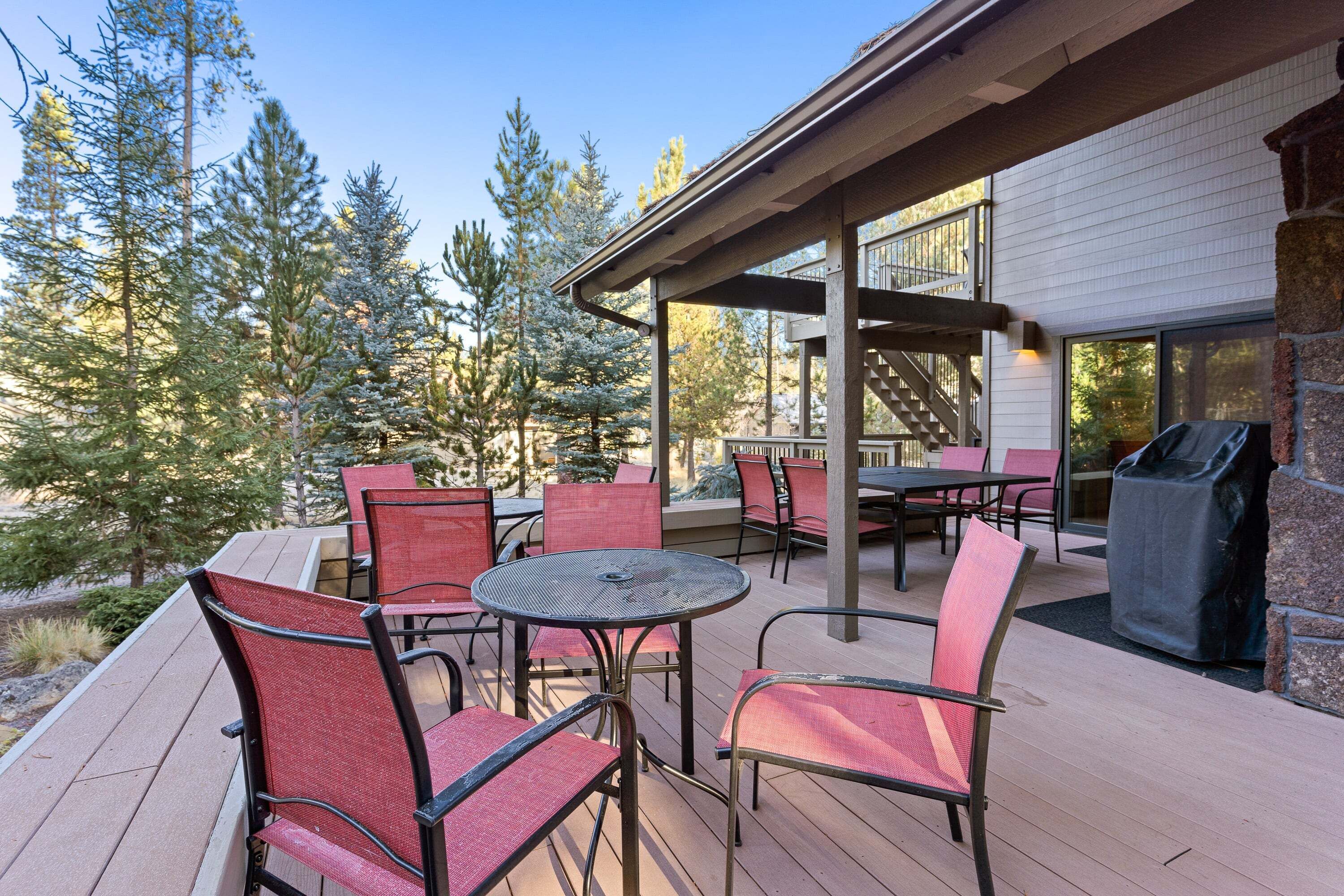 A deck with outdoor seating, a grill, and a view of trees.