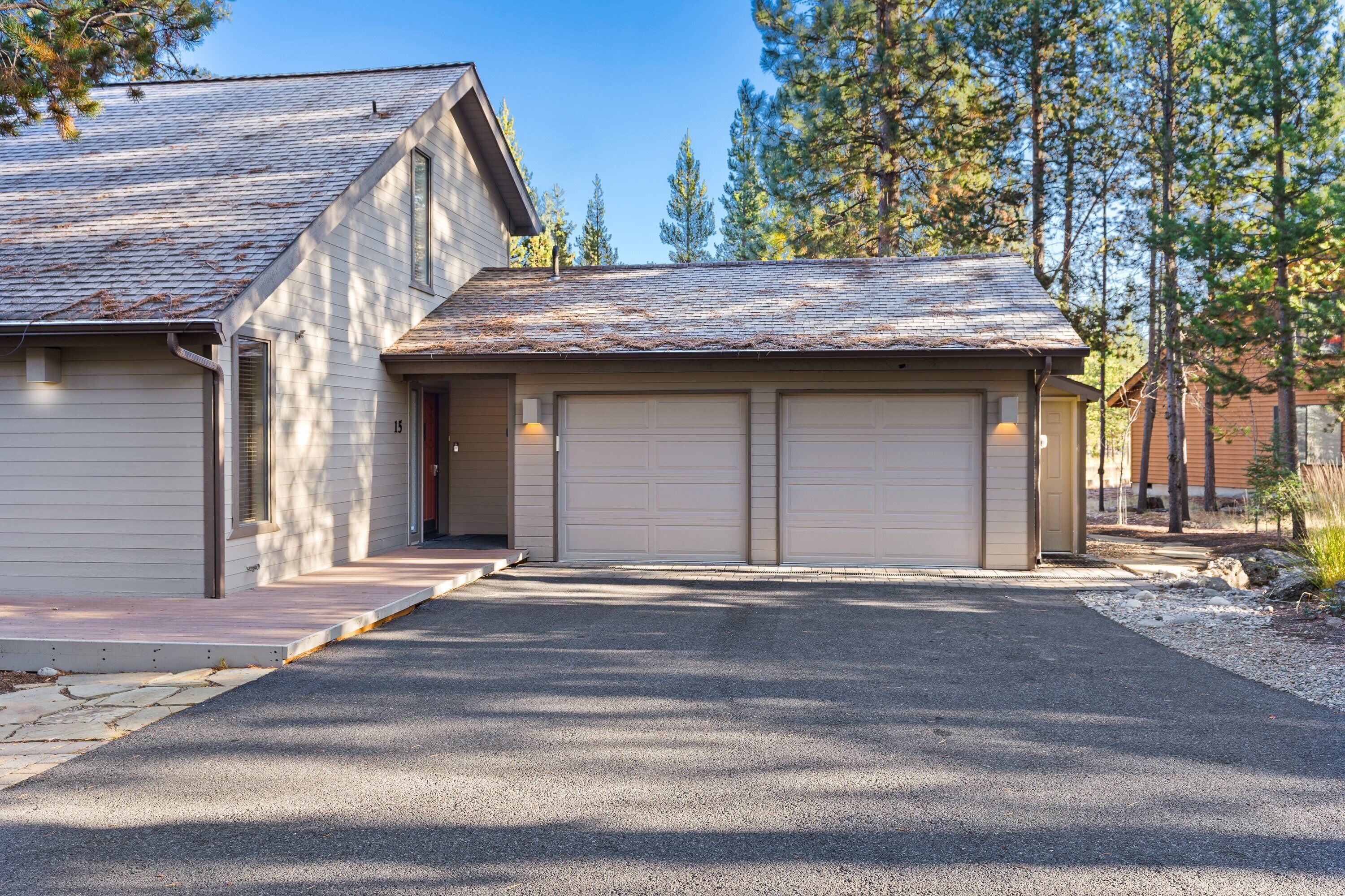 A two-story house with a garage, a driveway, and a small front yard with trees.
