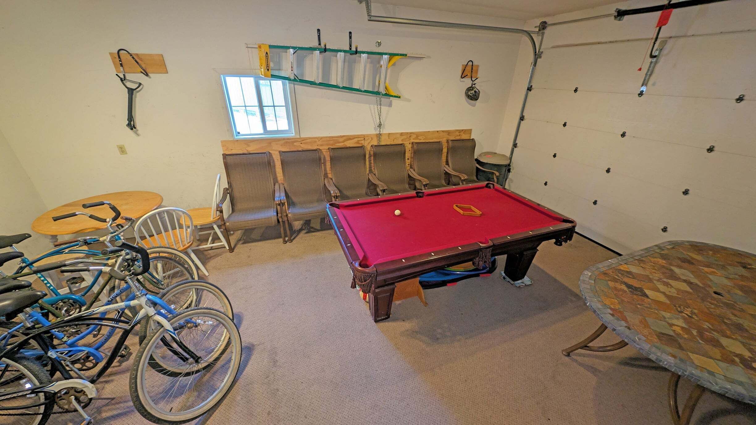 A room with a pool table, chairs, bicycles, and a window.