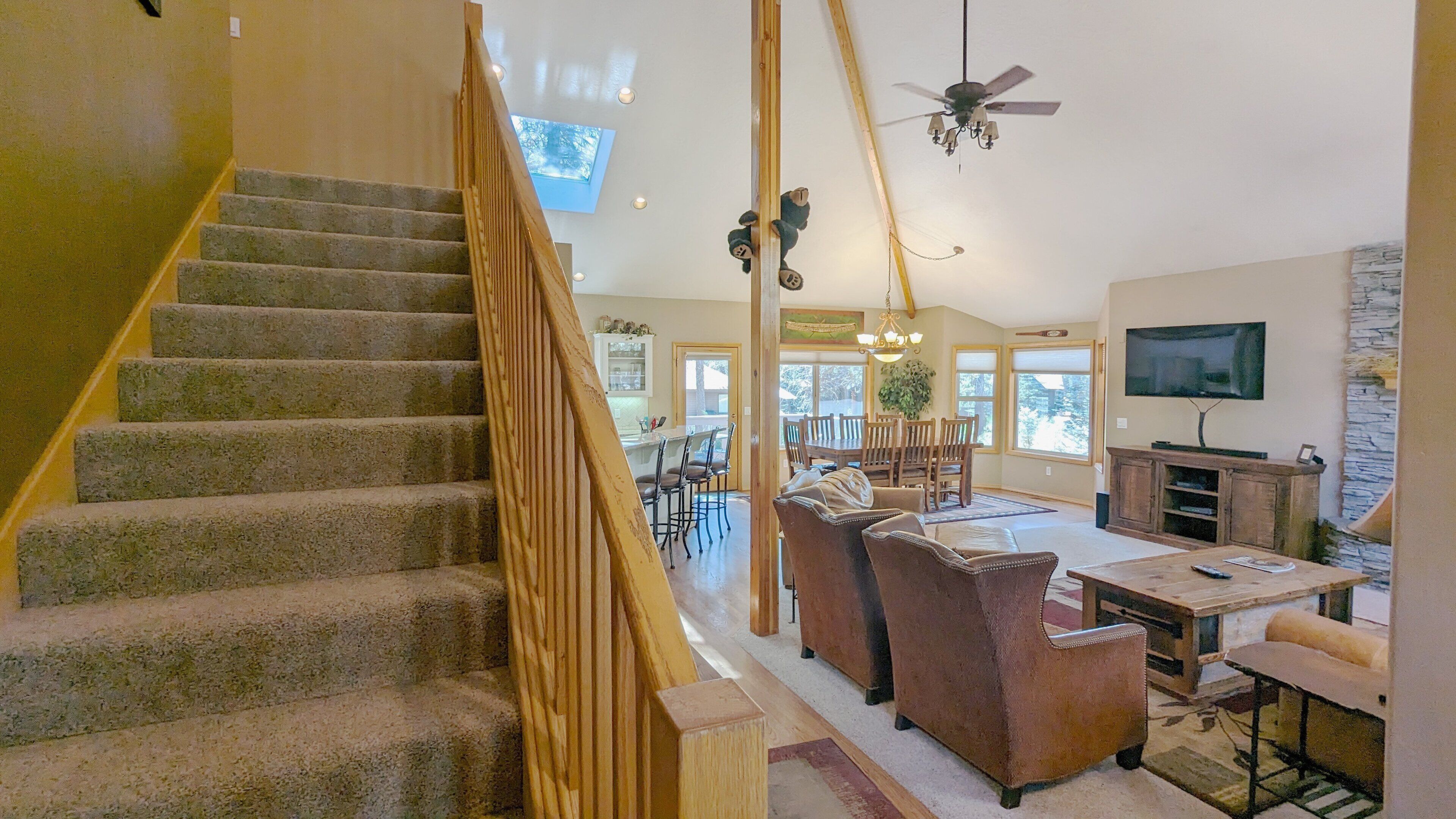 A staircase with a wooden handrail, a dining area with a table and chairs, a television mounted on the wall, and a ceiling fan.