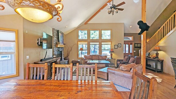 A spacious living area with a wooden floor, a stone fireplace, a large window, and a ceiling fan. - Mcnary 20 (Bend)