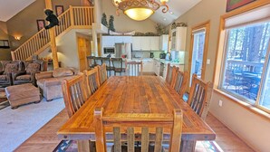 A spacious dining area with a long wooden table and chairs, a staircase leading to an upper level, and a view of the outdoors through a large window. - Mcnary 20 (Bend)