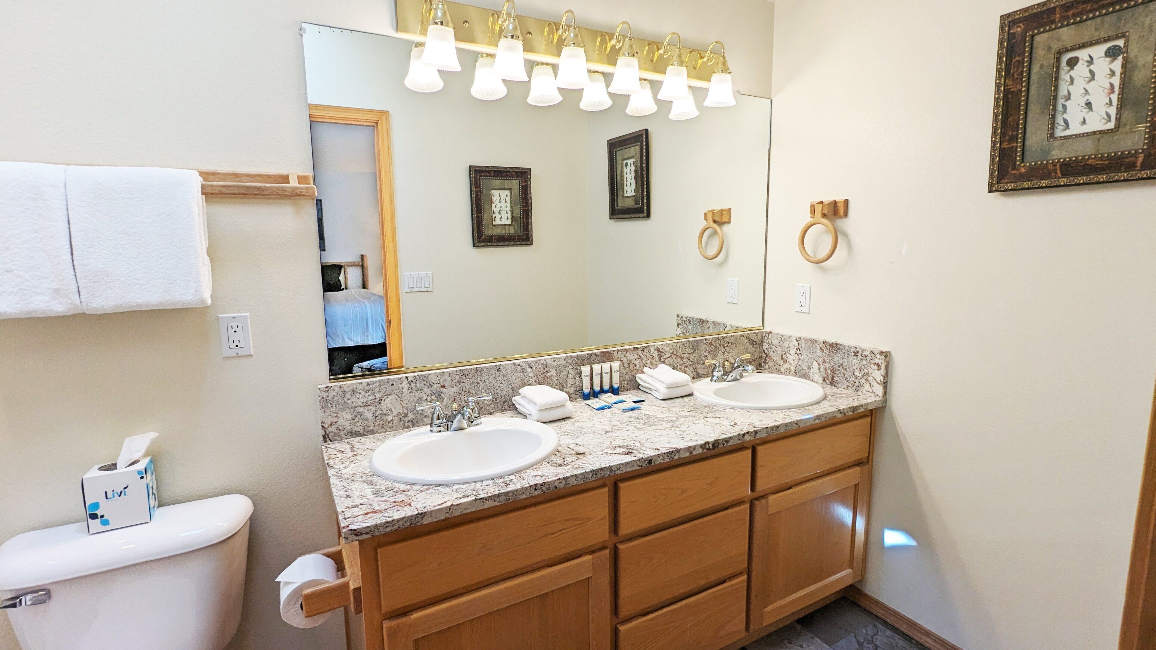 A bathroom with two sinks, a toilet, a mirror, and a towel rack.