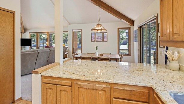 A kitchen with a granite countertop, wooden cabinets, a dining area with a table and chairs, and large windows. - Tokatee 1 (Bend)