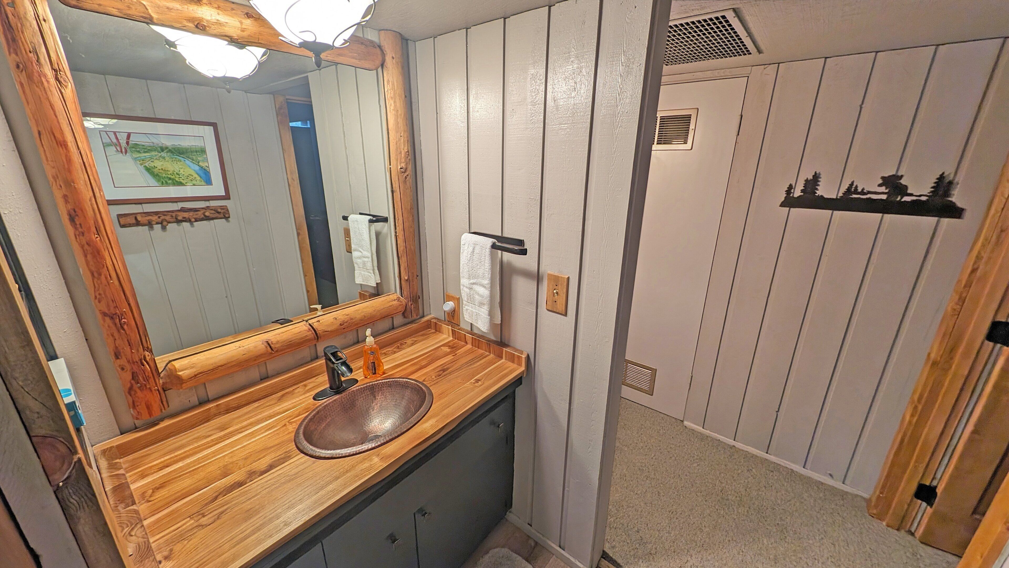 Ein Badezimmer mit einem Holzkosmetikschrank, einem Waschbecken, einem Spiegel und einem Handtuchhalter.