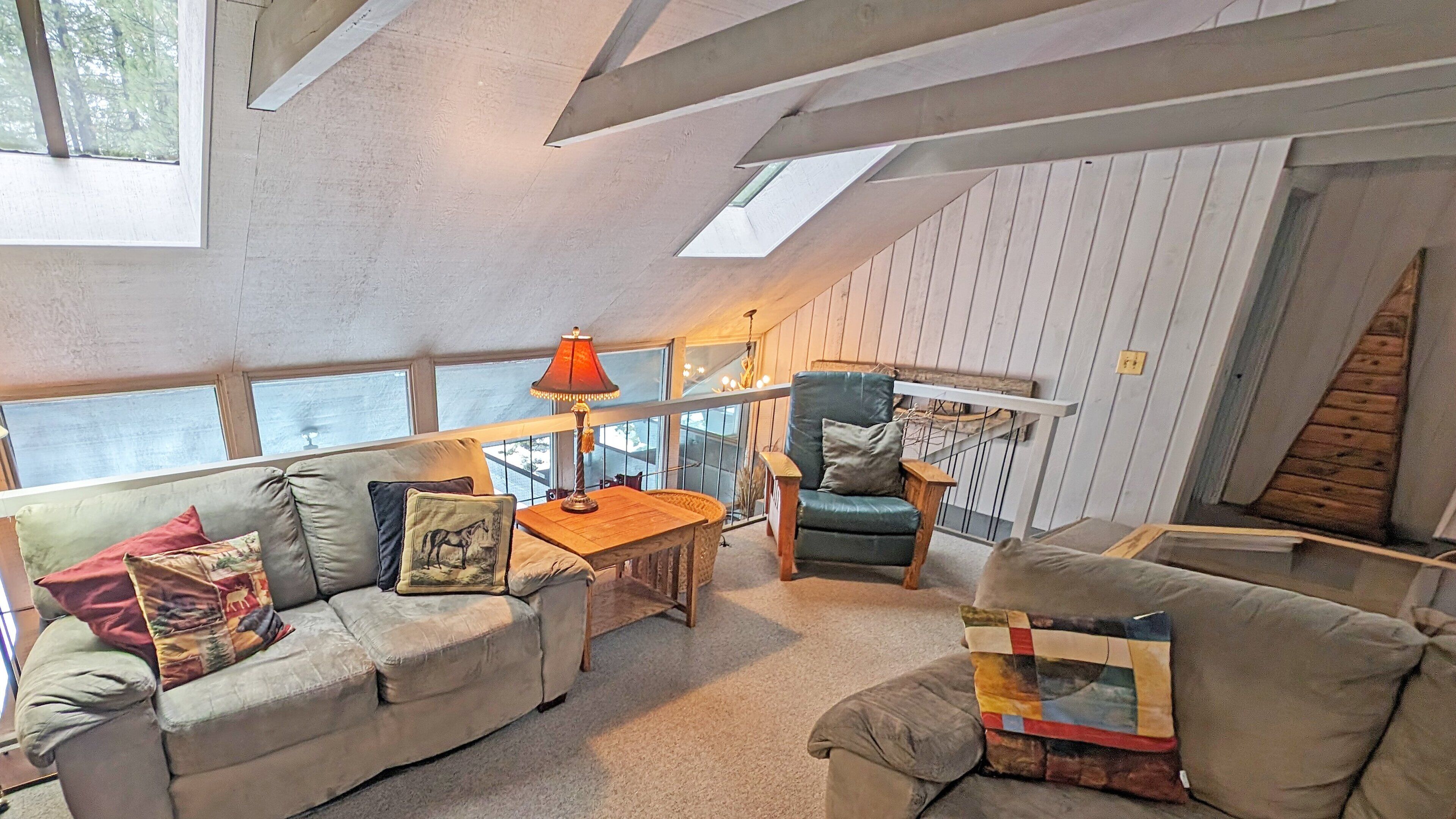 A loft-style room with a high ceiling, a sofa, a chair, a table, and a lamp.
