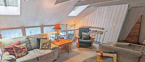 A loft-style room with a high ceiling, a sofa, a chair, a table, and a lamp.