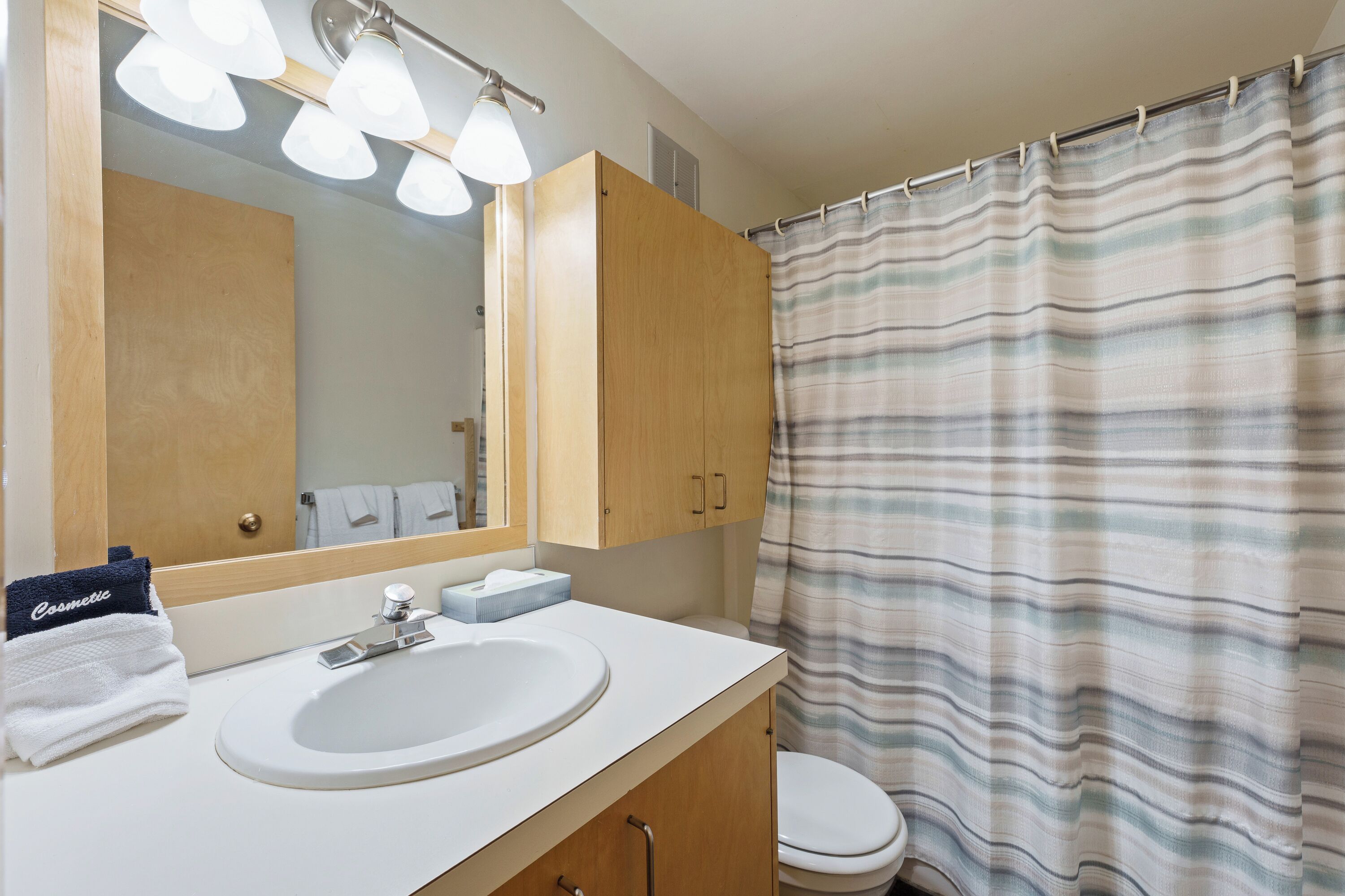 A bathroom with a white sink, wooden cabinets, a mirror, and a striped shower curtain.