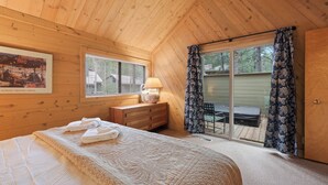A wooden cabin bedroom with a bed, a dresser, a lamp, and a sliding glass door to a patio.