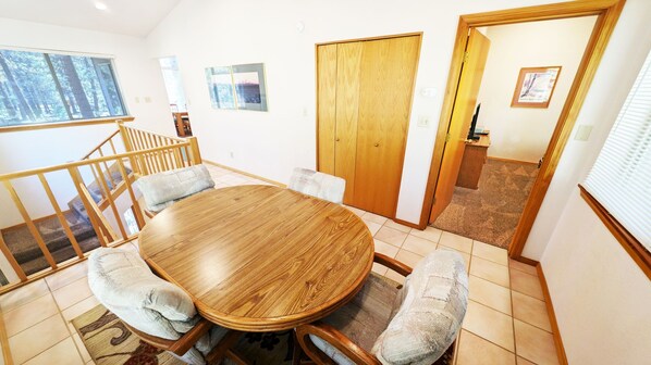 A dining area with a wooden table and cushioned chairs, a wooden staircase, and a view through a window. - Mt Hood 13 (Bend)