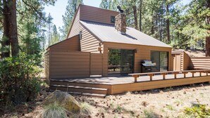 Una cabaña con terraza, chimenea y ventana con vista a un bosque.