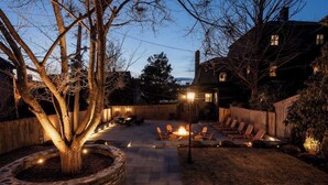A backyard with a fire pit, outdoor seating, and a stone planter with a tree. - Sanctuary Suite at The Royce, Newport (Newport)