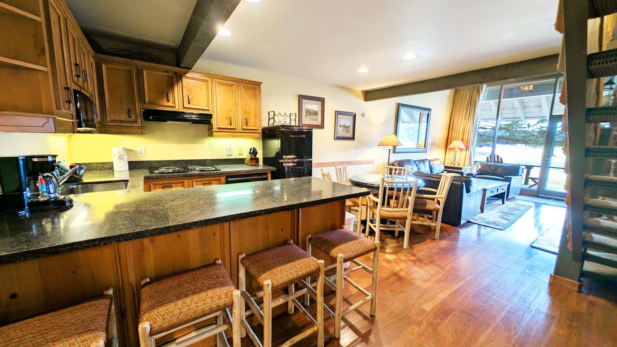 A kitchen with wooden cabinets, a black refrigerator, a stove, and a bar area with stools.