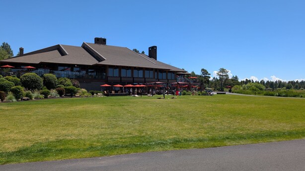 A large building with a flat roof, multiple windows, and outdoor seating with red umbrellas. - Mt Bachelor Retreat - 221 (Bend)