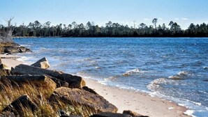 A coastal beach with rocky outcrops, a sandy shoreline, and a forested background. - 3 Blocks to Bay + Boat Parking + Renovated + 3 Bd (Lynn Haven)