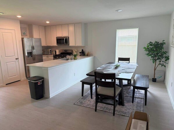 A modern kitchen with white cabinets, a central island, and a dining area with a table and chairs.