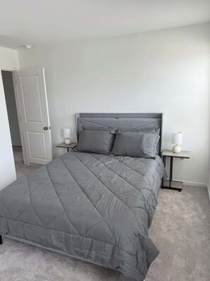 A bedroom with a grey bed, white walls, a door, and two bedside tables with lamps.