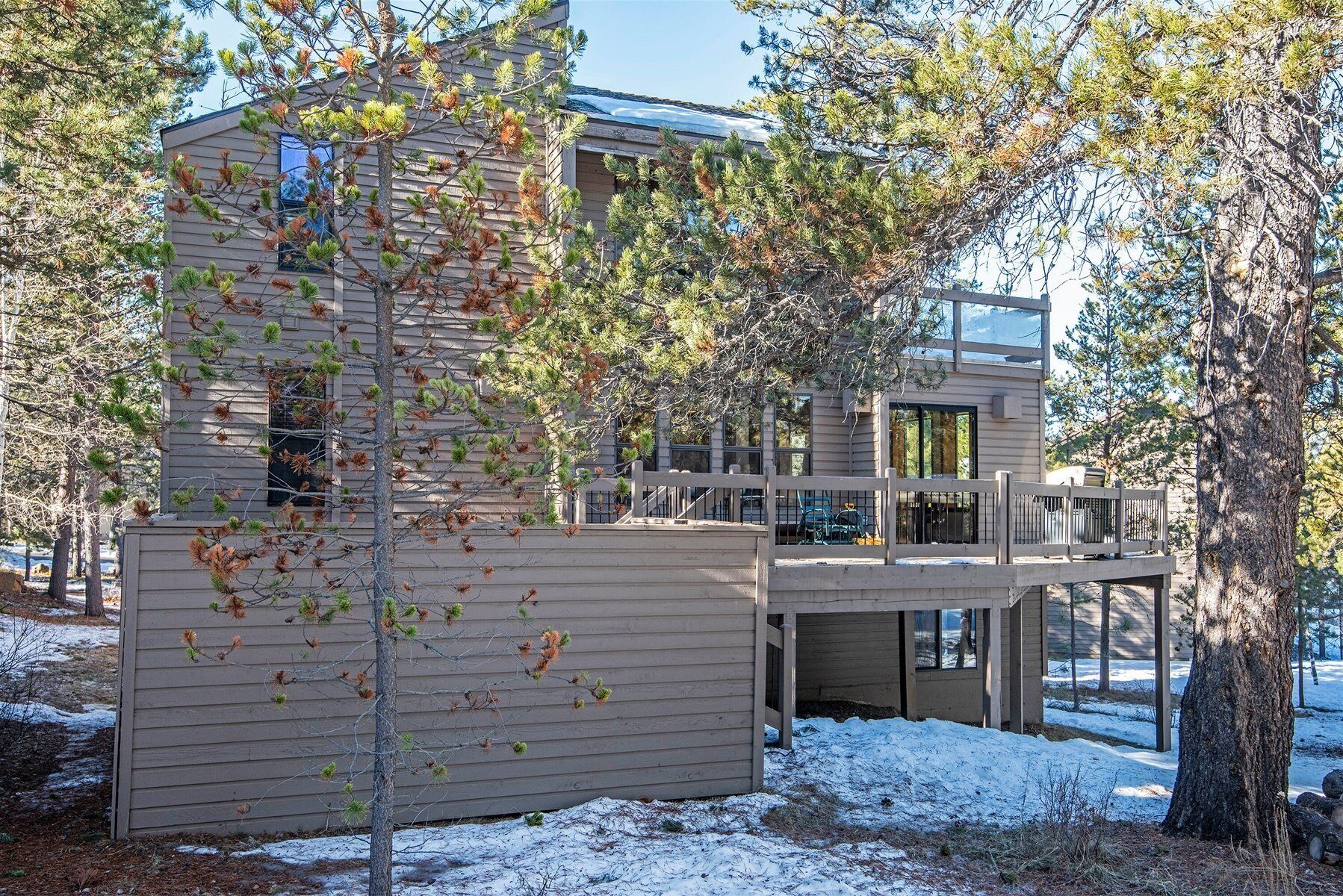Una moderna casa a due piani con una veranda, circondata da alberi e neve.