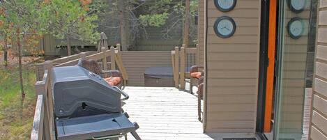 A deck with a grill, outdoor furniture, and a house with clocks on the wall.