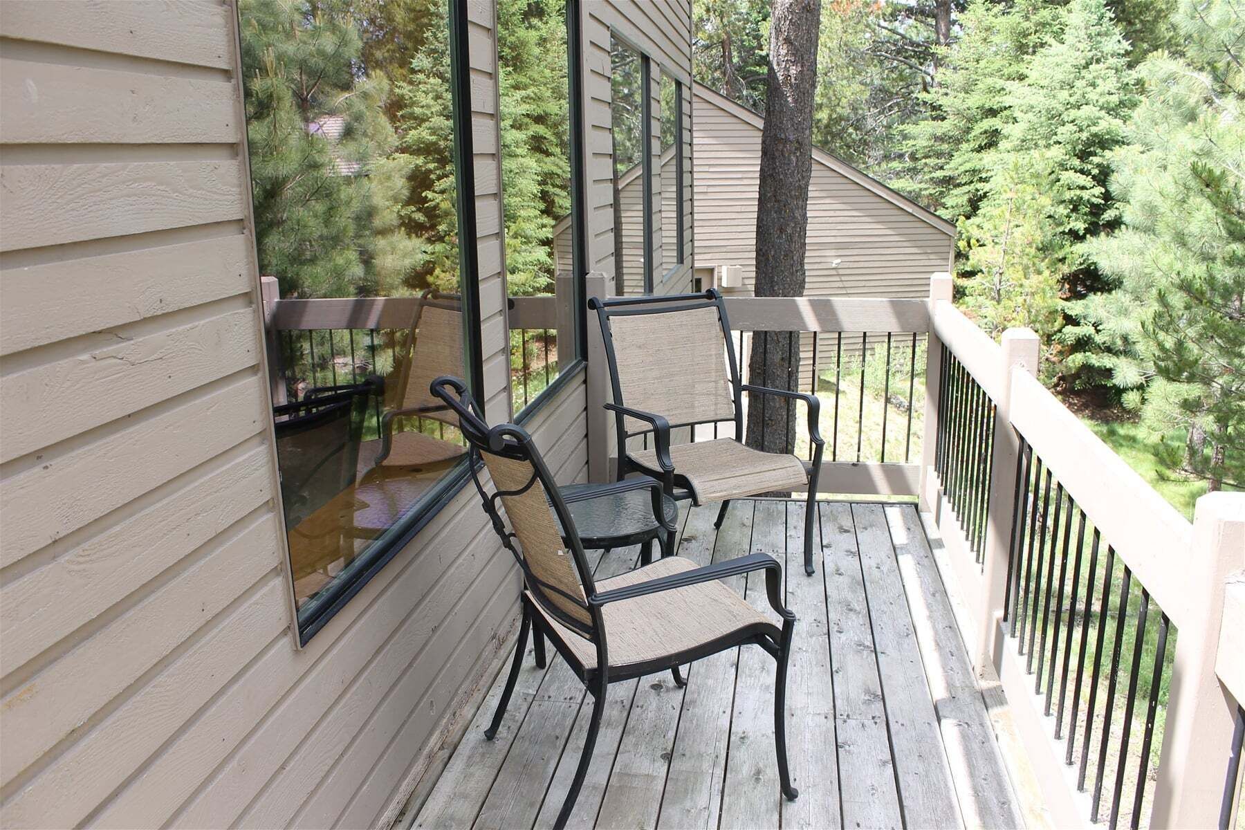 A wooden deck with two chairs and a table, overlooking a forested area.