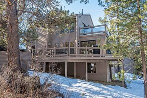 Une cabane en bois à deux étages, dotée d’un balcon, entourée d’arbres et de neige.