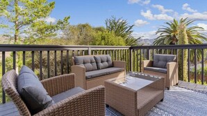 Ein Balkon mit Rattanmöbeln, darunter eine Couch und zwei Sessel, sowie ein Couchtisch mit Glasplatte.