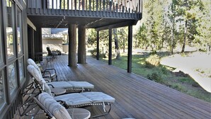 A covered outdoor deck with lounge chairs and a table, overlooking a natural landscape. - Goldfinch 3 (Bend)