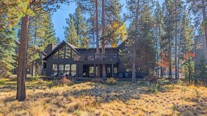 A cabin with a large deck, surrounded by tall trees and dry grass. - Goldfinch 3 (Bend)