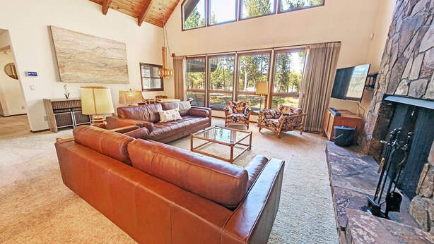 A spacious living room with a large brown leather sofa, a glass coffee table, and a stone fireplace. - Goldfinch 3 (Bend)