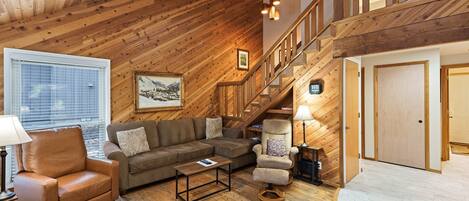 A wooden interior with a staircase, a sofa, a chair, and a table.