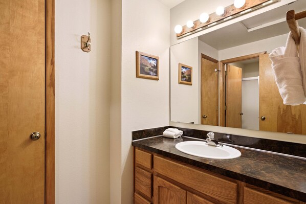 A bathroom with a wooden door, a sink, a mirror with lights, and two framed pictures on the wall. - Sequoia 14 (Bend)
