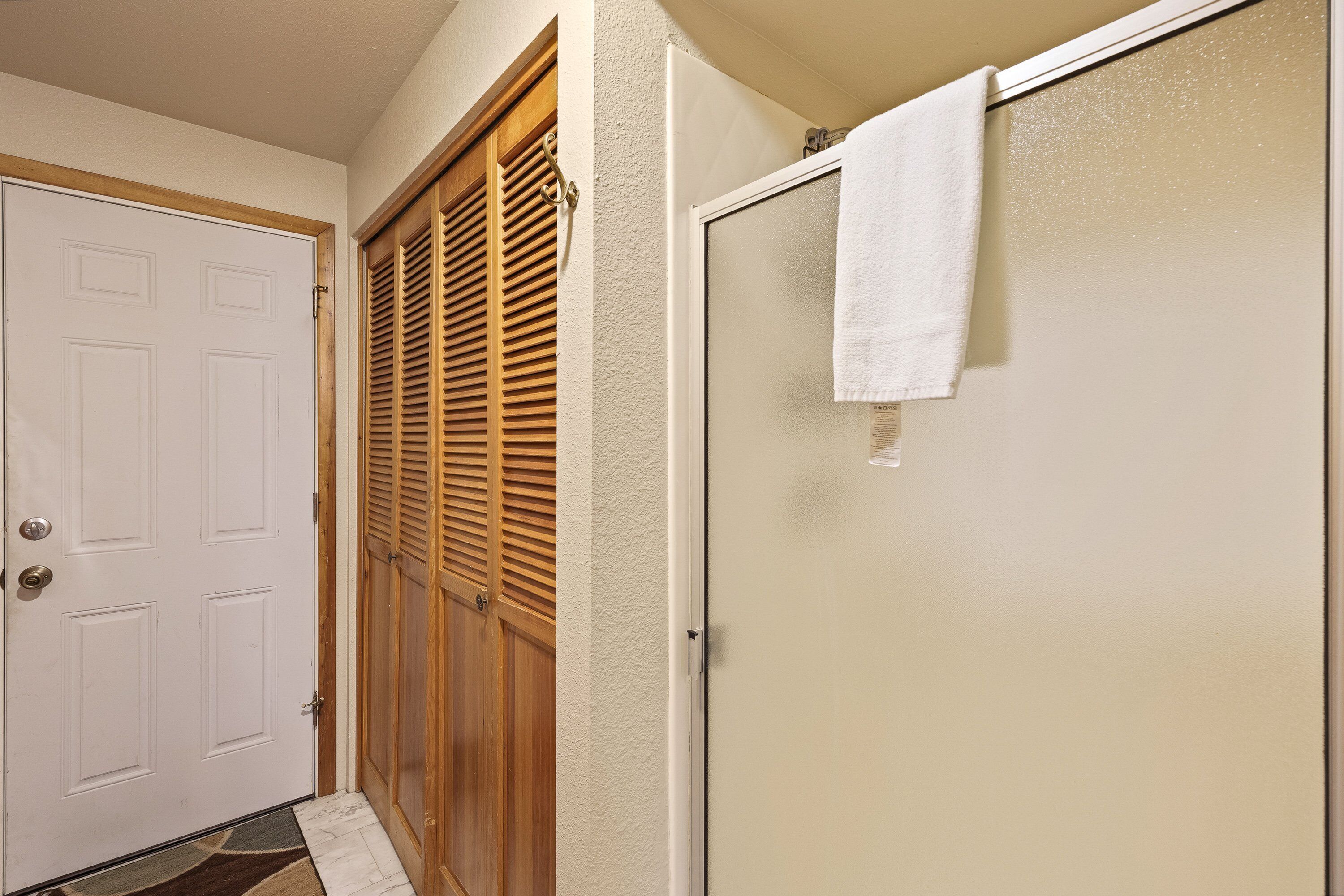 A bathroom with a shower, a white door, and a wooden door with louvered panels.