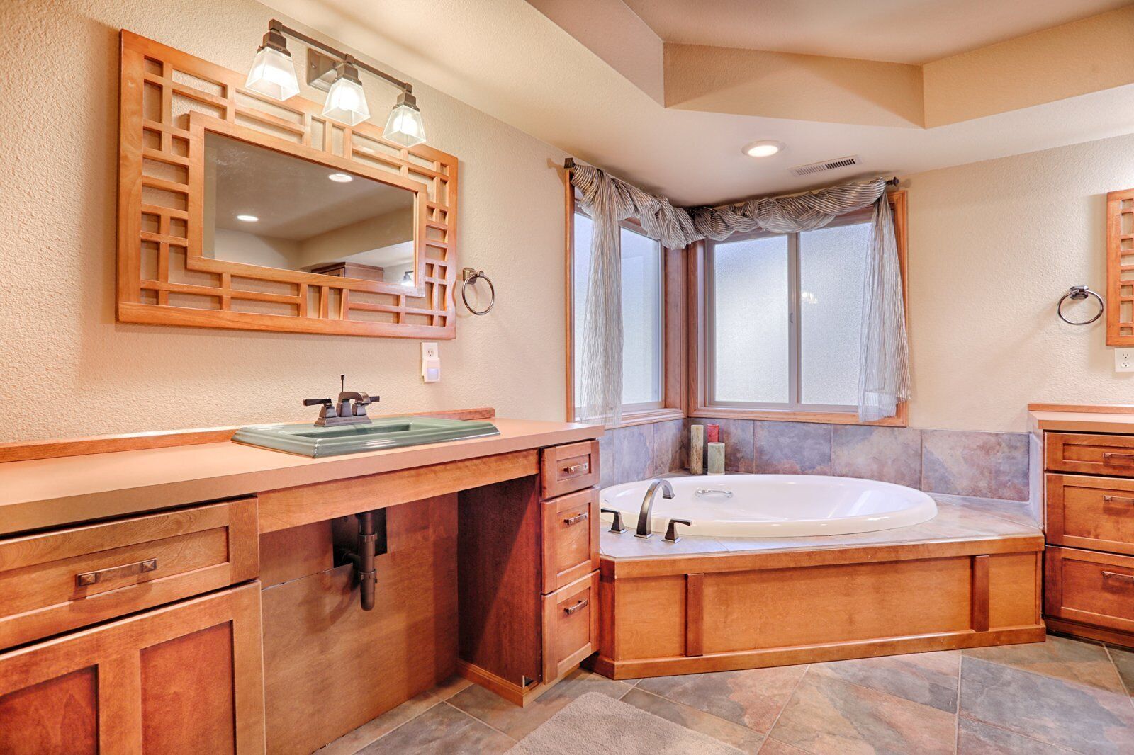 A spacious bathroom with a large bathtub, wooden vanity, and a mirror with lights.