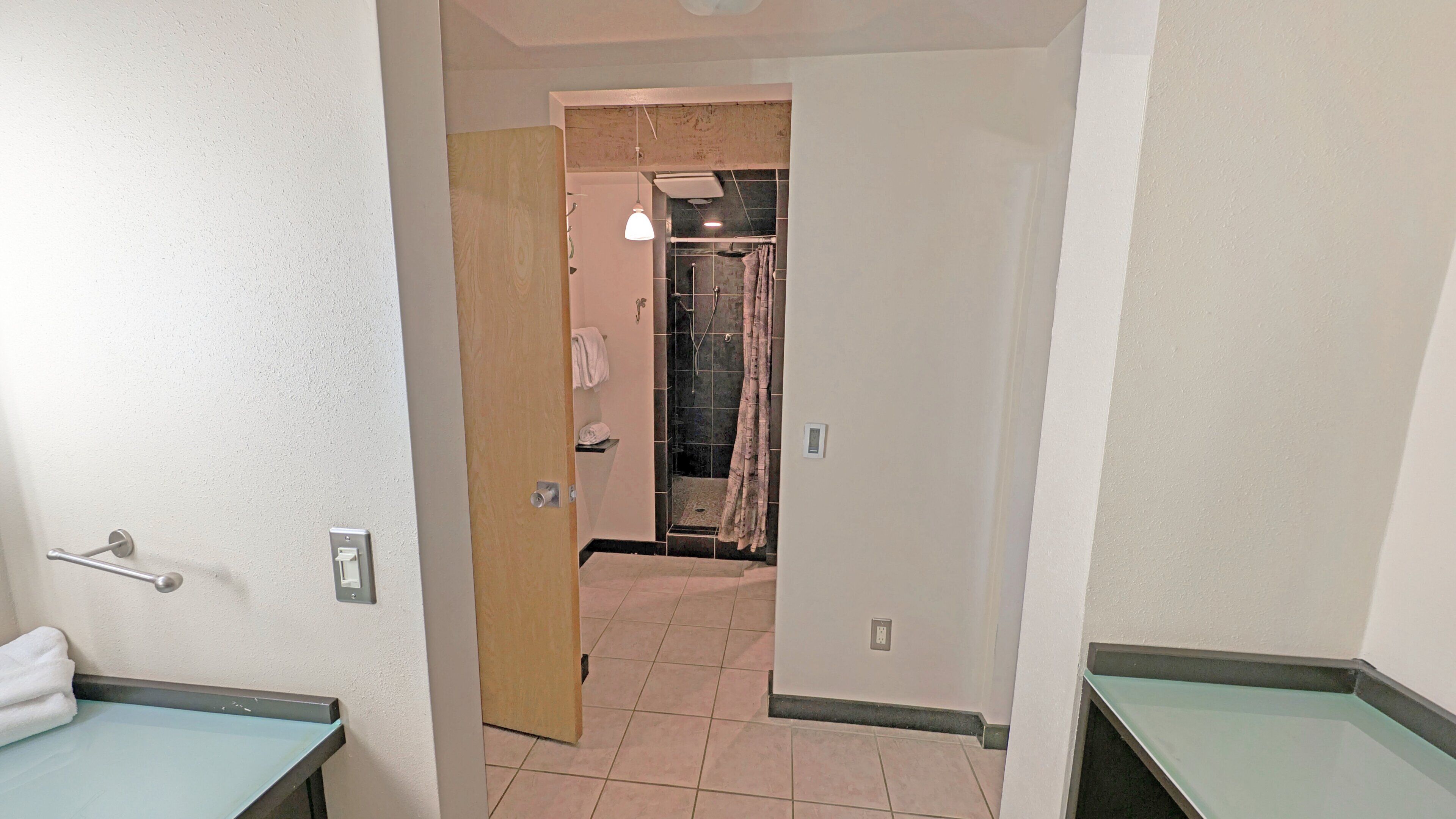 A hallway leading to a bathroom with a shower, a towel rack, and a light fixture.