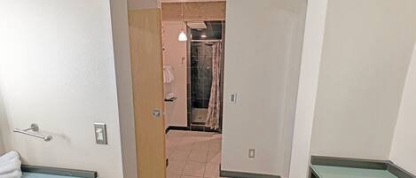 A hallway leading to a bathroom with a shower, a towel rack, and a light fixture.