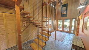 Una escalera de madera con un diseño moderno que lleva a una habitación con piso de piedra y un gran ventanal.