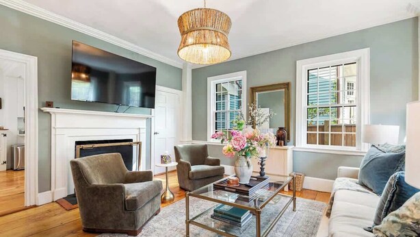A living room with a fireplace, a television mounted above it, and a large window with blinds. - Regatta Suite at The Royce Refined Newport Charm (Newport)